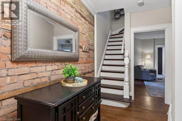 Entryway hall with exposed brick, dresser, mirror, and view of the staircase and living room. - 427 Jackson Street W, Hamilton
