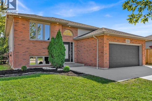 Close-up front view of a brick house with landscaping, a covered porch, and a gray garage door. - 4274 Dennison Court, Windsor