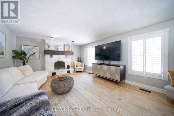 Living room with beige sectional sofa, white brick fireplace, and light wood floors. - 428 Charlotteville Road 1, Norfolk