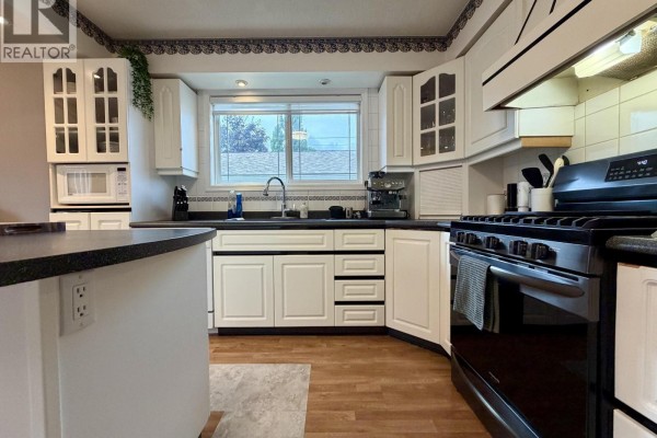 Kitchen with white cabinets, black countertops, and a window above the sink. - 4280 First Avenue, Smithers