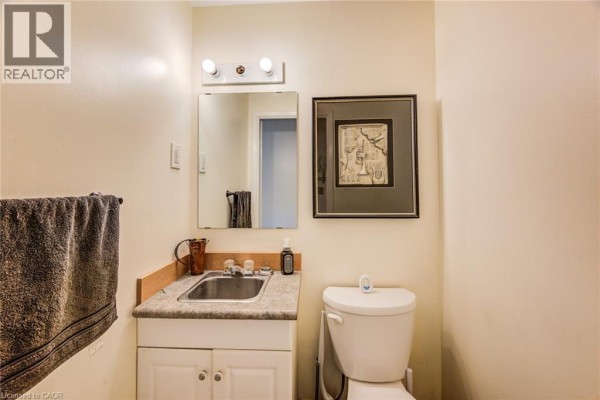 Powder room with a toilet, vanity sink, mirror, and framed artwork on the wall. - 428b Dunvegan Drive, Waterloo