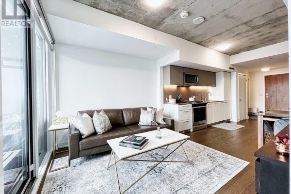 Living area with a leather sofa, marble coffee table, and open-concept kitchen. - 429 - 30 Baseball Place, Toronto