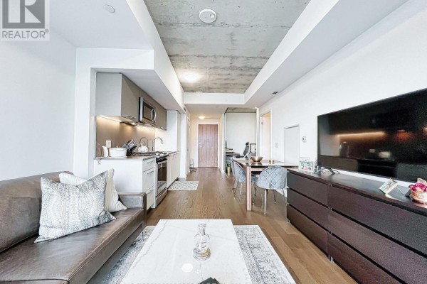 Living room with sofa, kitchen, dining area, and large television on dresser. - 429 - 30 Baseball Place, Toronto