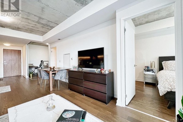 View of the living room, dining area, and open bedroom door with bed. - 429 - 30 Baseball Place, Toronto