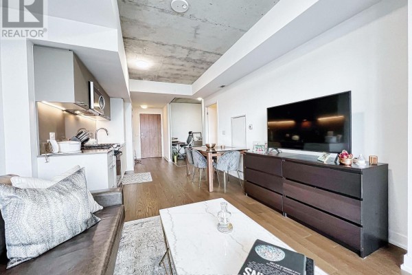 Living area with sofa, kitchen, dining area, and dark wood dresser with TV. - 429 - 30 Baseball Place, Toronto