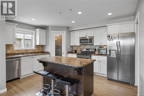 Kitchen with white cabinets, granite countertops, stainless steel appliances, and a dark wood island with seating. - 429 Alpen Way, Nanaimo
