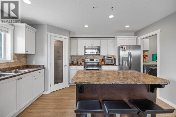Spacious kitchen featuring white cabinetry, stainless steel appliances, a central island, and a pantry door. - 429 Alpen Way, Nanaimo