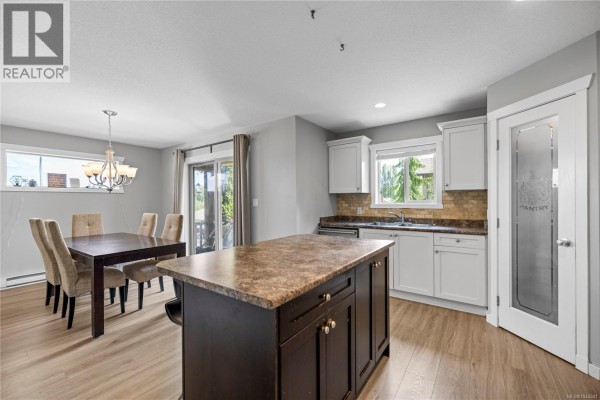 Dining area with a dark wood table and chairs, adjacent to the kitchen and a sliding glass door. - 429 Alpen Way, Nanaimo