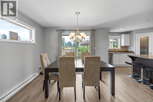Dining room with a table set for four, a chandelier, and a view of the backyard through the window. - 429 Alpen Way, Nanaimo