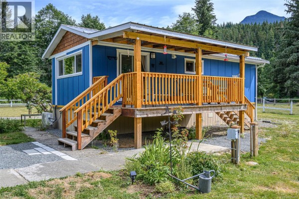 Blue house with covered porch, green lawn, and outdoor furniture. - 429 Community Rd, Sayward