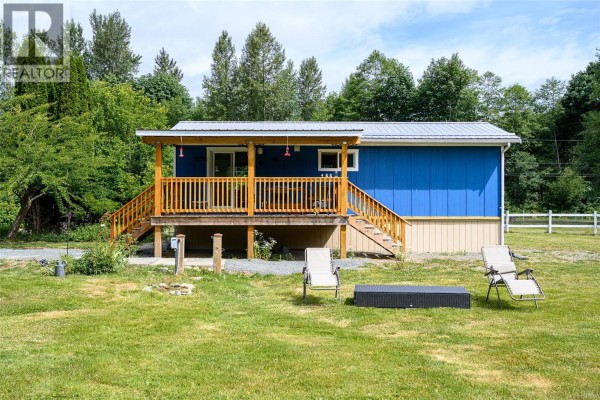 Covered wooden porch with chairs, table, and sliding glass door. - 429 Community Rd, Sayward