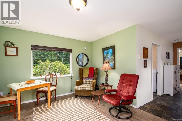 Kitchen with white appliances, wood cabinets, and living area with red chair. - 429 Community Rd, Sayward