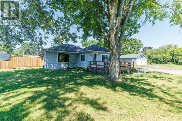 Side view of a light blue bungalow with a wooden deck, garage, and mature tree. - 429 Delaware Avenue, Fort Erie
