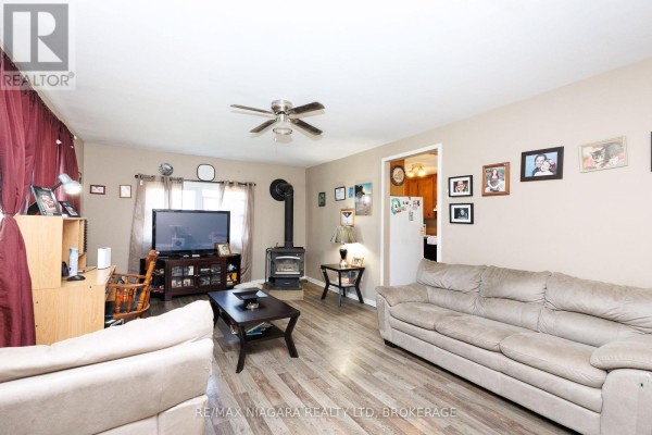 Living room with two sofas, a wood stove, television, and light wood laminate flooring. - 429 Delaware Avenue, Fort Erie