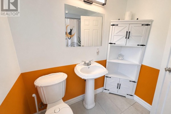 Bathroom with a white pedestal sink, toilet, and a tall white corner cabinet. - 429 Grenfell Crescent, Labrador City