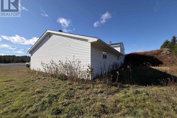 Side view of the house with overgrown grass and shrubs - 429 Highway 7, Ecum Secum