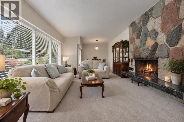 Living room with a large stone fireplace, two couches, coffee table, and dining room in the background. - 429 Newlands Road, West Vancouver