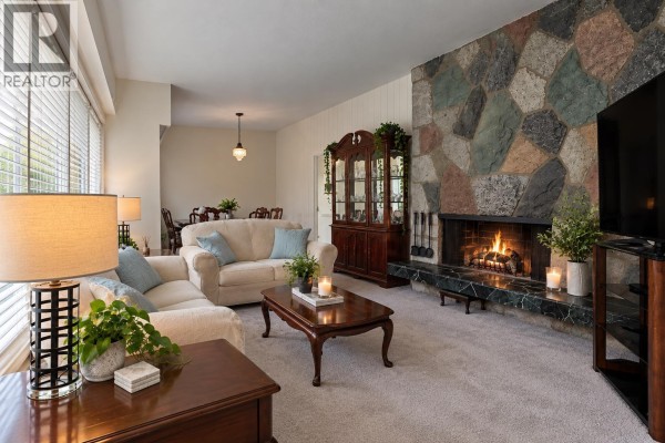 Living room with a stone fireplace, large windows, two couches, and a wooden display cabinet. - 429 Newlands Road, West Vancouver