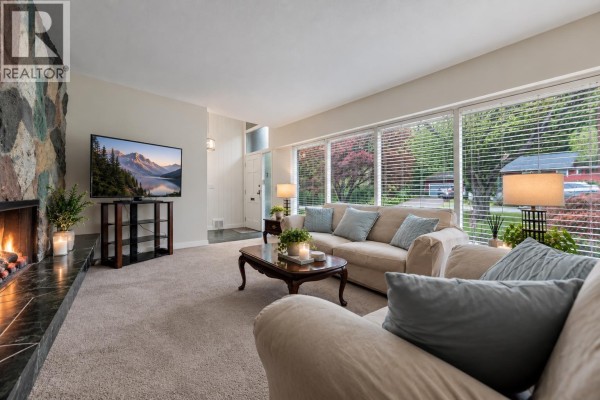 Living room with a stone fireplace, TV, large windows overlooking the street, and a front door. - 429 Newlands Road, West Vancouver