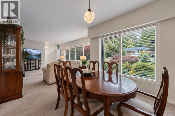 Dining room with a wooden table and six chairs, large windows, and a view of the living room. - 429 Newlands Road, West Vancouver