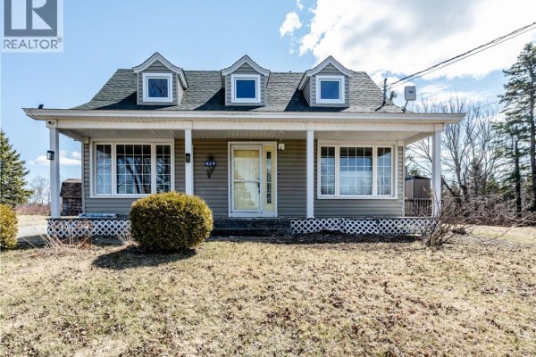 Front view of a light grey house with dormer windows, a covered porch with white railings, and a manicured bush. - 429 Saint-athanase, Rogersville