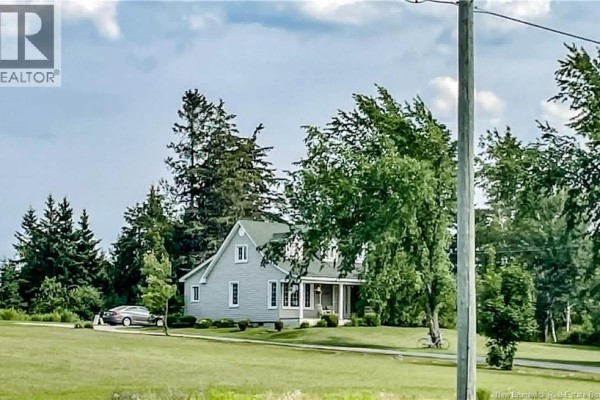 Distant view of a light grey house with a gabled roof, surrounded by green trees and a car parked in the driveway. - 429 Saint-athanase, Rogersville