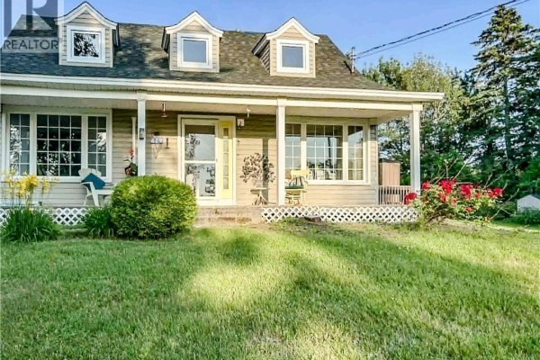 Front view of a light grey house with a covered porch, yellow door, dormer windows, and red roses blooming by the porch. - 429 Saint-athanase, Rogersville