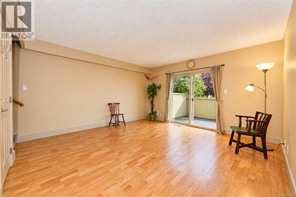 Empty living room with laminate flooring, beige walls, and sliding glass door. - 43 4061 Larchwood Dr, Saanich
