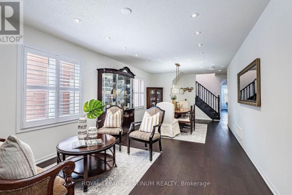 Living and dining area with dark hardwood floors, white walls, plantation shutters, chairs, and a staircase. - 43 Arkwright Drive, Brampton