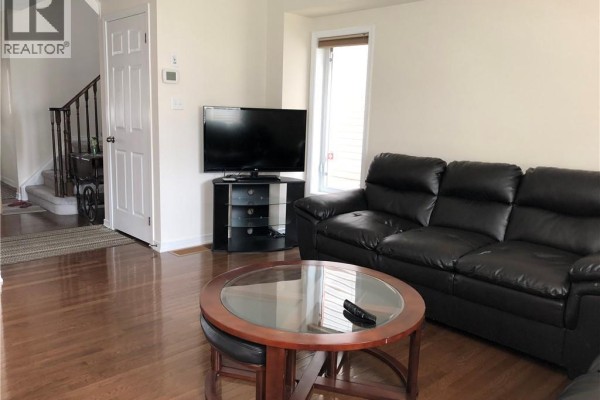 Living room with a black leather sofa, television on a stand, and hardwood floors, looking towards the entryway. - 43 Armstrong Avenue, Cambridge
