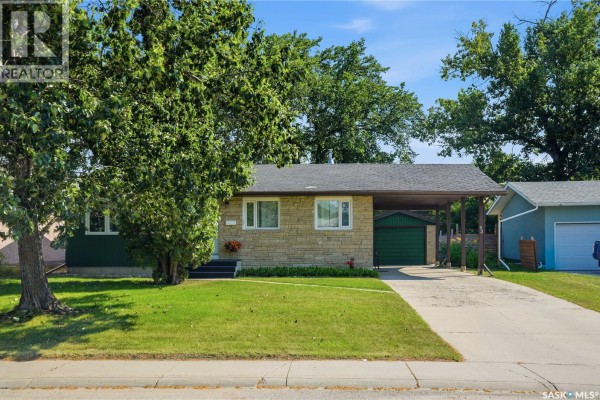 Front view of the bungalow with a large tree in the foreground. - 43 Columbia Drive, Saskatoon