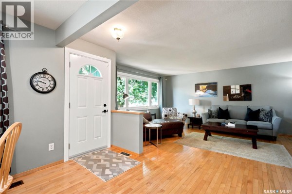 Living room with hardwood floors, grey walls, a white front door, and large windows. - 43 Columbia Drive, Saskatoon