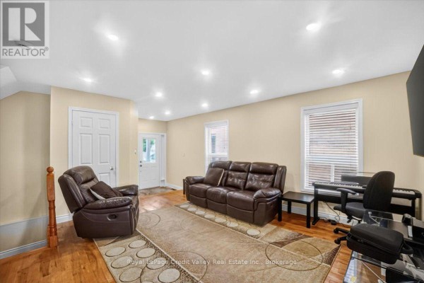 Living room with leather furniture, a piano, and a front entrance door. - 43 Coppermill Drive, Brampton
