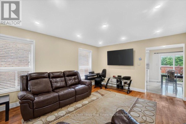 Living room with leather furniture, a TV, and a view into a dining area. - 43 Coppermill Drive, Brampton