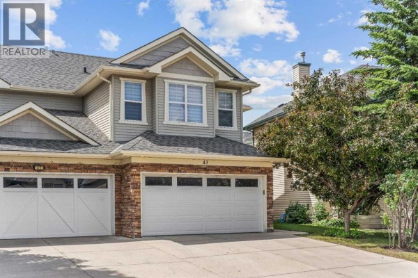 Front exterior of a duplex with a double garage and stone accents on a sunny day. - 43 Cougar Ridge Bay Sw, Calgary