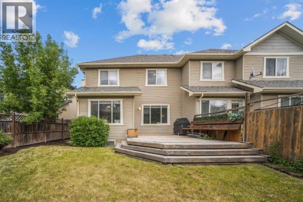Backyard of a duplex with a wooden deck and green grass. - 43 Cougar Ridge Bay Sw, Calgary