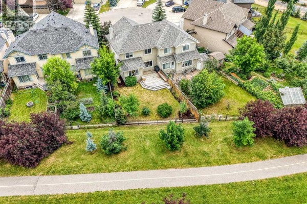 Aerial view of a duplex with a large green backyard and surrounding trees. - 43 Cougar Ridge Bay Sw, Calgary