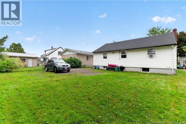 Rear exterior of the bungalow with a green grassy yard, gravel driveway, and shed. - 43 Derby Street, Moncton
