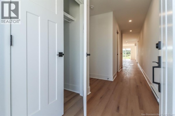 Interior hallway with white doors, hardwood floors, and natural light from rooms at the end. - 43 Downsview Drive, Saint John