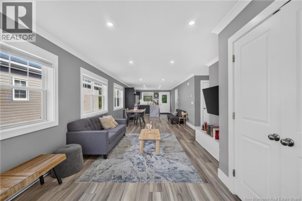 Open concept living room with grey walls, wood-look floors, and view of kitchen. - 43 Eatman Avenue, Fredericton