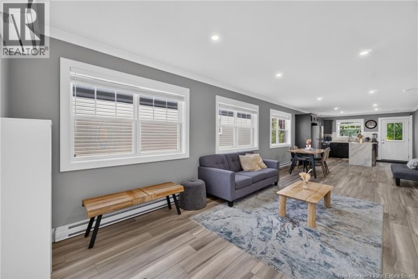 Living area with grey sofa, wooden bench, and view of dining area and kitchen. - 43 Eatman Avenue, Fredericton