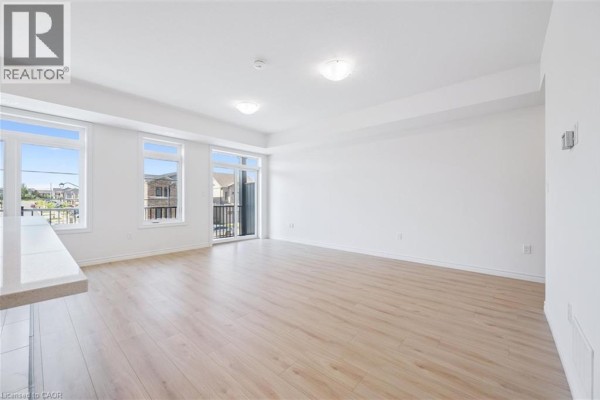 Empty living room with light wood floors, white walls, and large windows overlooking the neighborhood. - 43 Lomond Lane, Kitchener