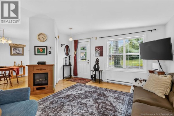 Living room featuring a fireplace, large rug, brown sofa, blue chair, and dining area beyond. - 43 Sequoia Drive, Moncton