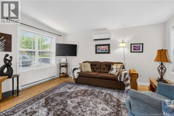 Living room with a brown sofa, air conditioning unit, large rug, and a window view. - 43 Sequoia Drive, Moncton