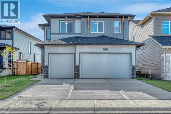 Front exterior of a two-story house during the day, featuring a double garage, paved driveway, and a pitched roof. - 43 South Shore Road, Chestermere