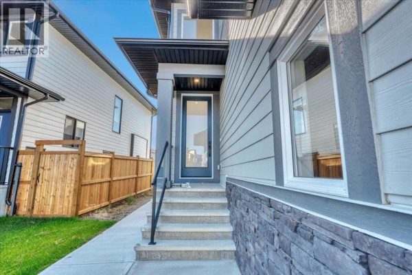 Entrance to a modern house with a glass door, concrete steps, and decorative stone siding. - 43 South Shore Road, Chestermere