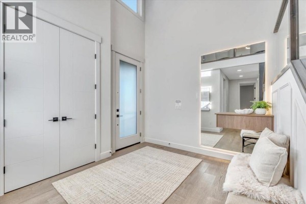 Foyer with white double doors, a glass entry door, and a large illuminated mirror above a bench and console table. - 43 South Shore Road, Chestermere