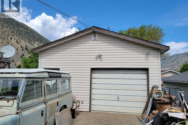 Exterior of a detached garage with a roll-up door and a vintage vehicle parked beside it. - 430 2nd Avenue, Keremeos