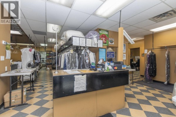 Interior view of a dry cleaning business reception area with a counter and clothes racks. - 430 7 Street Sw, Salmon Arm