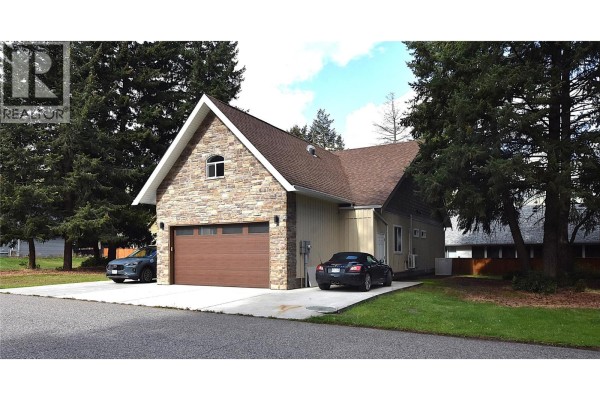Side view of a house showing a garage, stone facade, and parked cars on concrete driveway. - 430 Hummingbird Avenue, Vernon